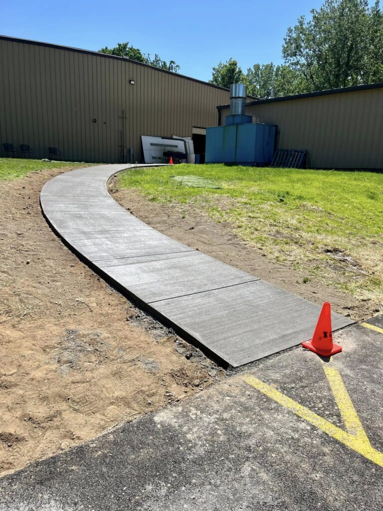 Xpress Construction & Services shows a freshly built sidewalk by a building, marking progress on concrete and landscaping work.
